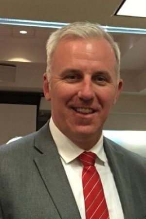 Jason Kelley, Chairman of the Board, smiles in front of a group of people.