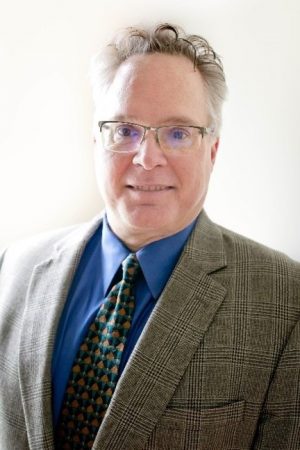 A man in glasses wearing a suit and tie, identified as Jason Kelley, Chairman of the Board.
